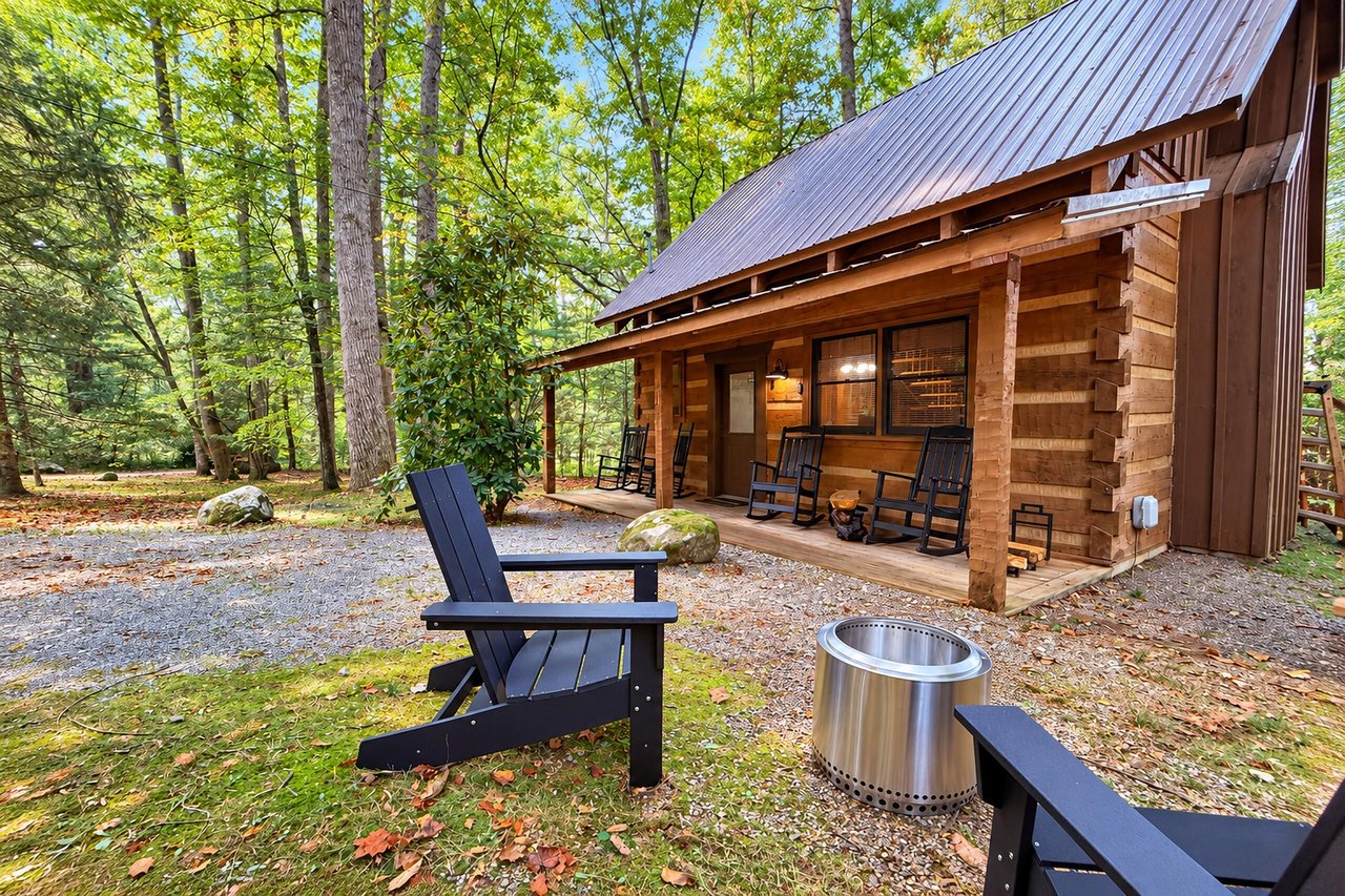 Charming log cabin nestled in lush forest surroundings, featuring a welcoming porch with rocking chairs and a fire pit perfect for evening relaxation.
