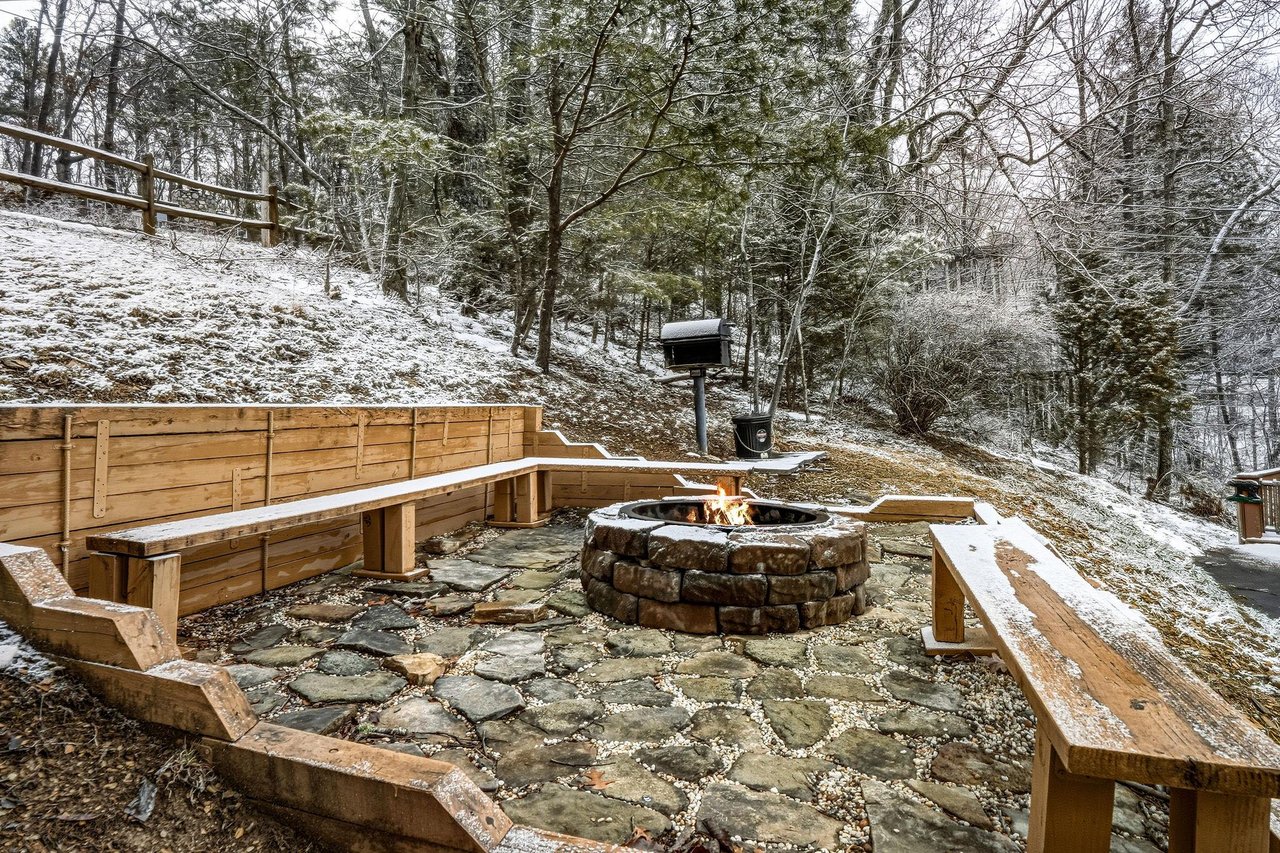 Gather around your private fire pit nestled in a snowy forest setting, complete with rustic stone seating for magical winter evenings.