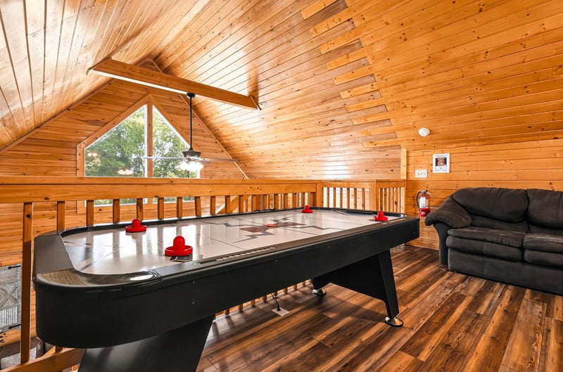Your loft game room awaits with air hockey and cozy seating, perfect for friendly competition and downtime under warm wooden beams with natural light streaming in.