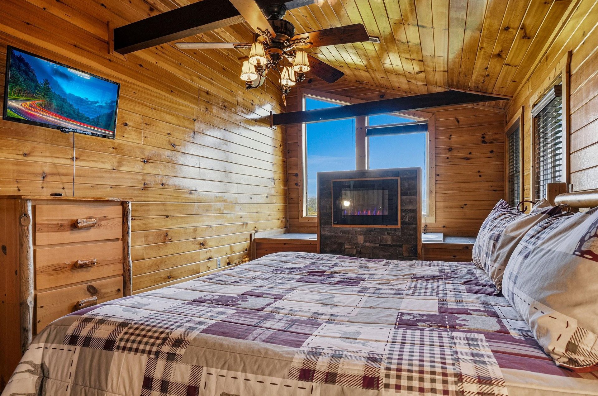Curl up in this warm, rustic bedroom where glowing wooden walls wrap around you, a cozy fireplace crackles at the foot of your bed, and your favorite shows await on the mounted TV.