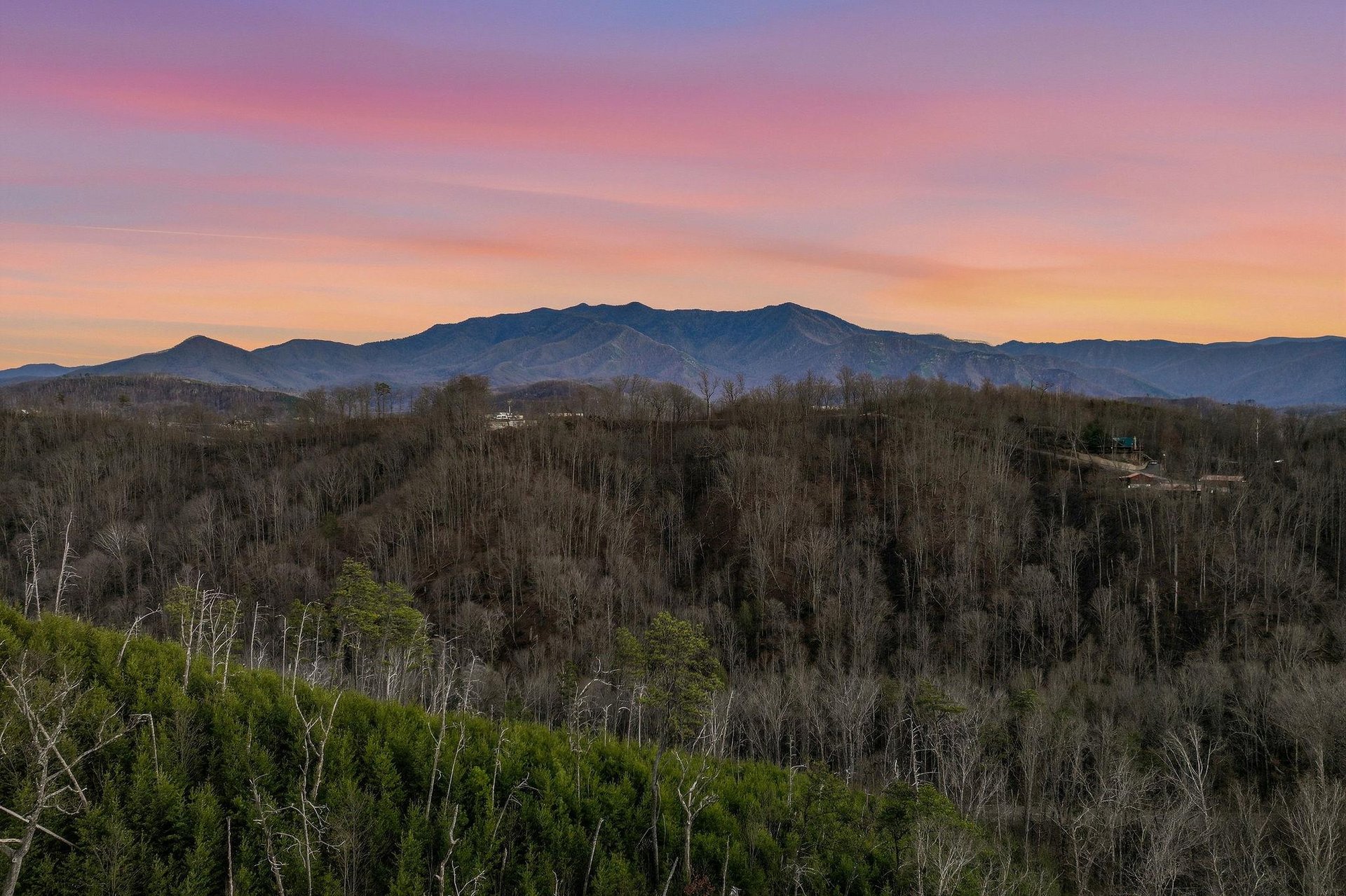 Stunning mountain panorama with vibrant sunset colors painting the sky over forested valleys and distant peaks.