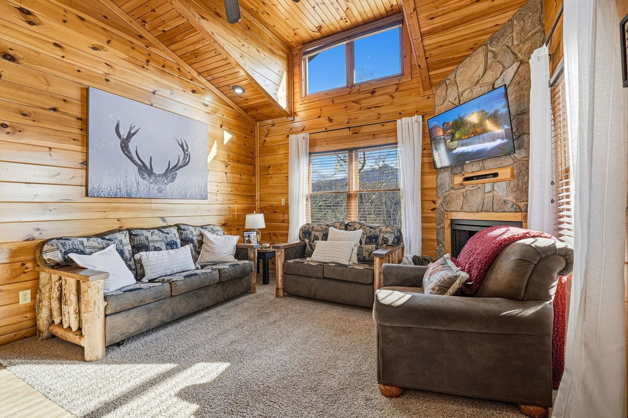 Sink into plush seating surrounded by warm wood and rustic charm, where your stone fireplace crackles beneath soaring ceilings and natural light.