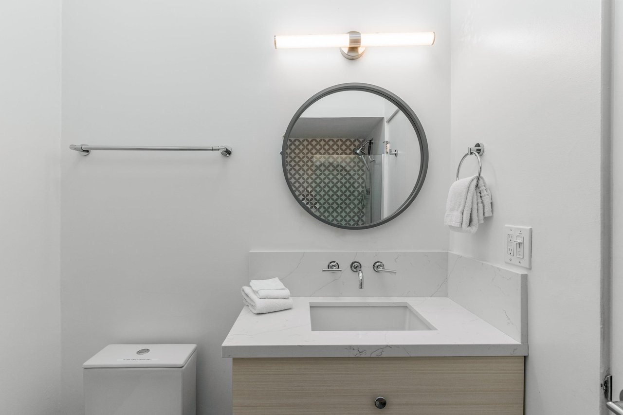 Fresh white towels await you in this bright, modern bathroom with stylish marble countertop and sleek fixtures.