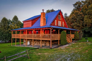 A striking red cabin with a wraparound deck set in a peaceful wooded setting, offering a private and scenic escape.