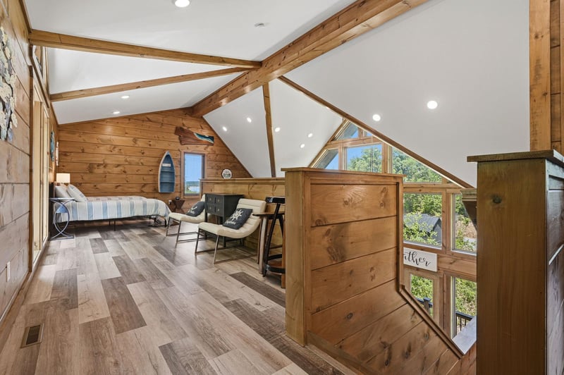Cozy loft bedroom with exposed wood beams and large windows offering natural light for your peaceful retreat.
