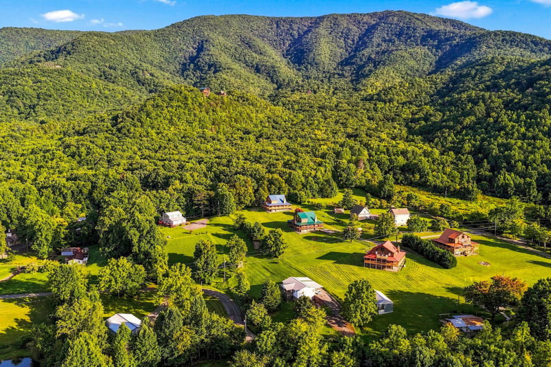 A peaceful mountain retreat surrounded by expansive wooded landscapes and open lawns, with cabins nestled at the base of forested ridges.