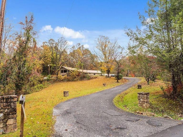 A scenic driveway winds through vibrant autumn foliage toward a welcoming property nestled among colorful trees.