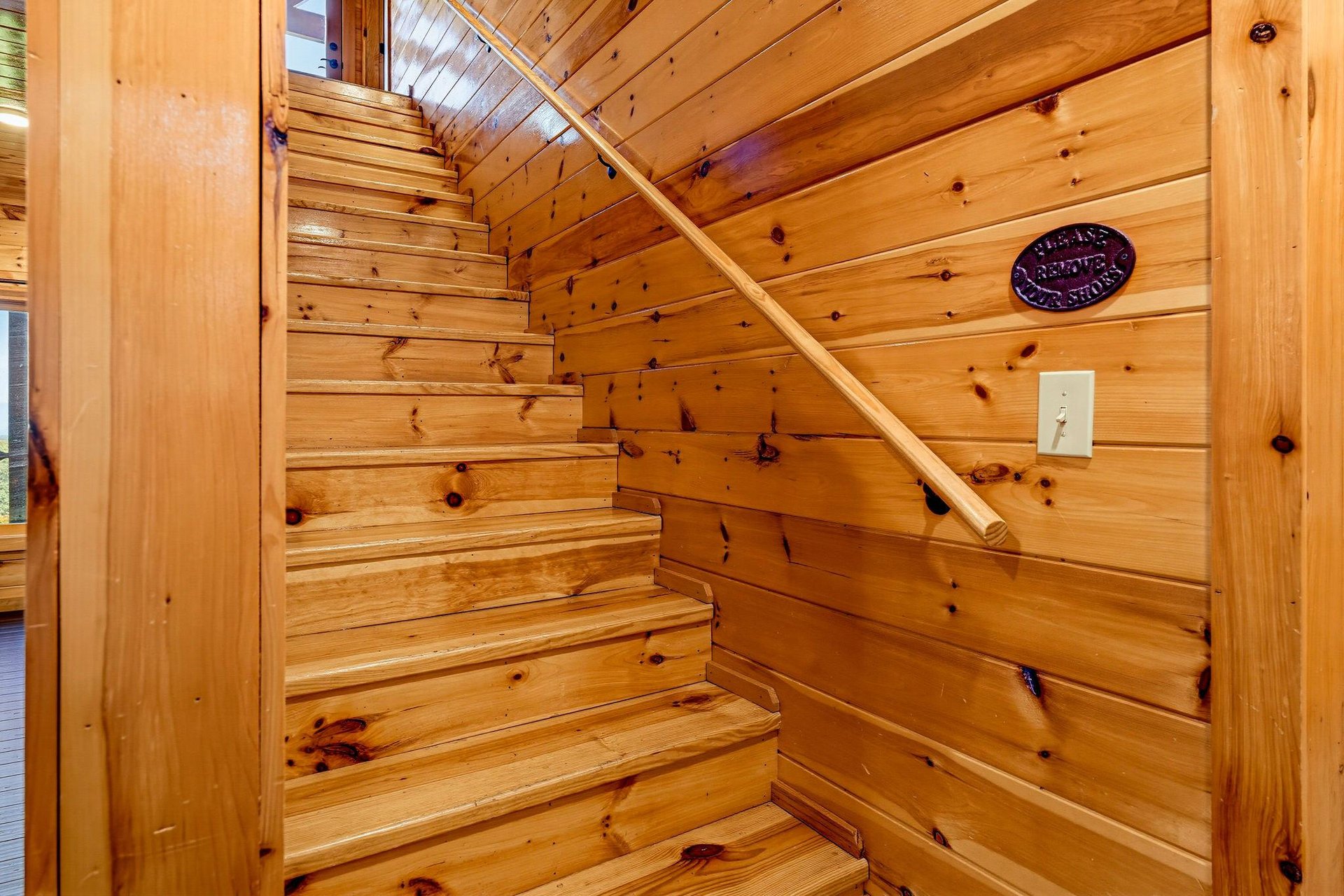 The warm wooden staircase leads you upward, surrounded by rustic pine walls and natural light from above, creating a cozy mountain retreat feel.
