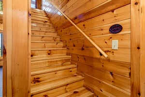 The warm wooden staircase leads you upward, surrounded by rustic pine walls and natural light from above, creating a cozy mountain retreat feel.