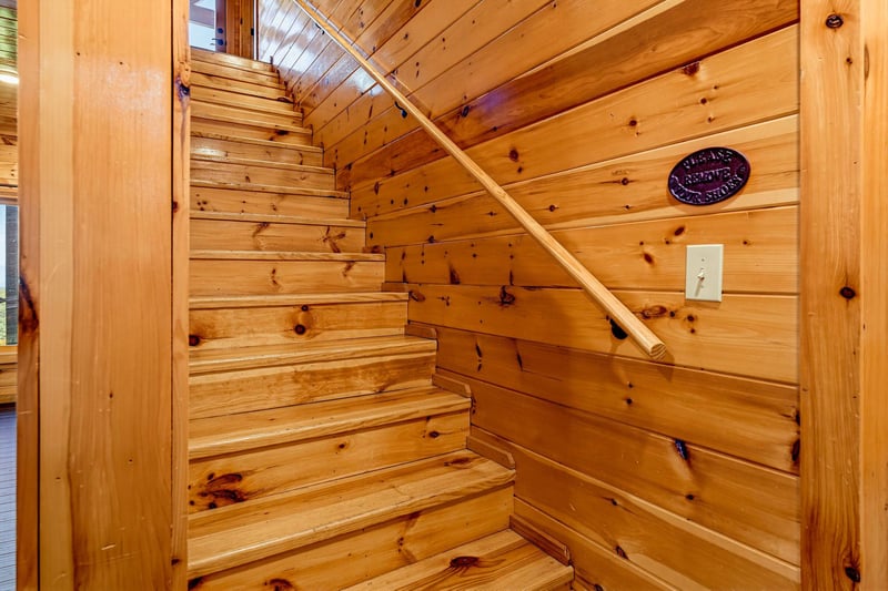 The warm wooden staircase leads you upward, surrounded by rustic pine walls and natural light from above, creating a cozy mountain retreat feel.