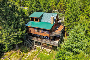 A welcoming mountain cabin nestled in lush forest, featuring wraparound decks and a striking green metal roof—perfect for secluded getaways surrounded by nature.