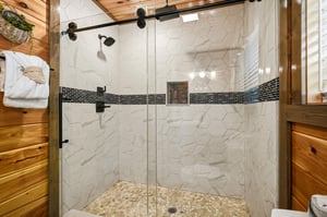 Step into your private spa with this stunning hexagonal marble shower featuring warm wood accents and modern glass doors.
