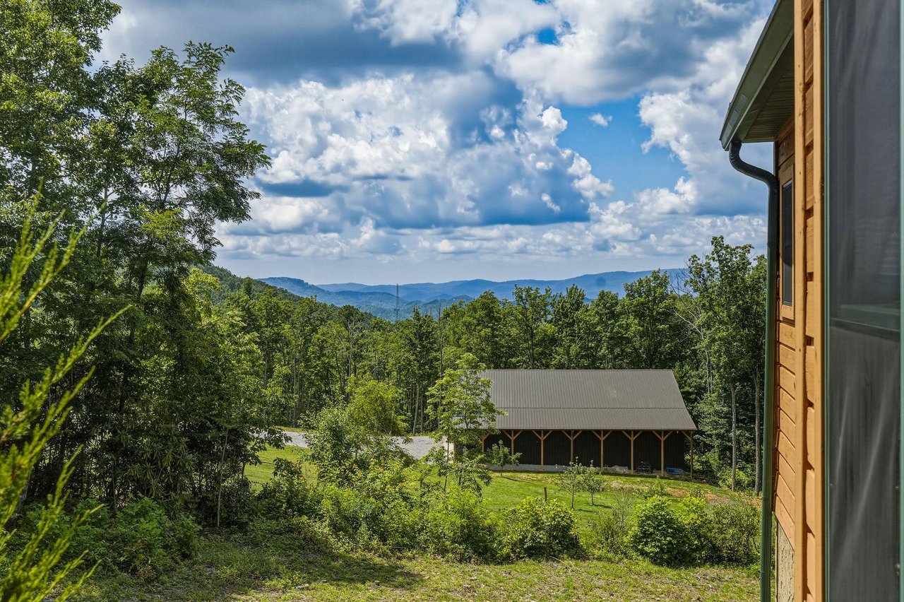 Mountain retreat nestled among rolling hills and lush forest, offering stunning views of layered mountain ranges beneath a dramatic sky—a peaceful destination surrounded by nature.