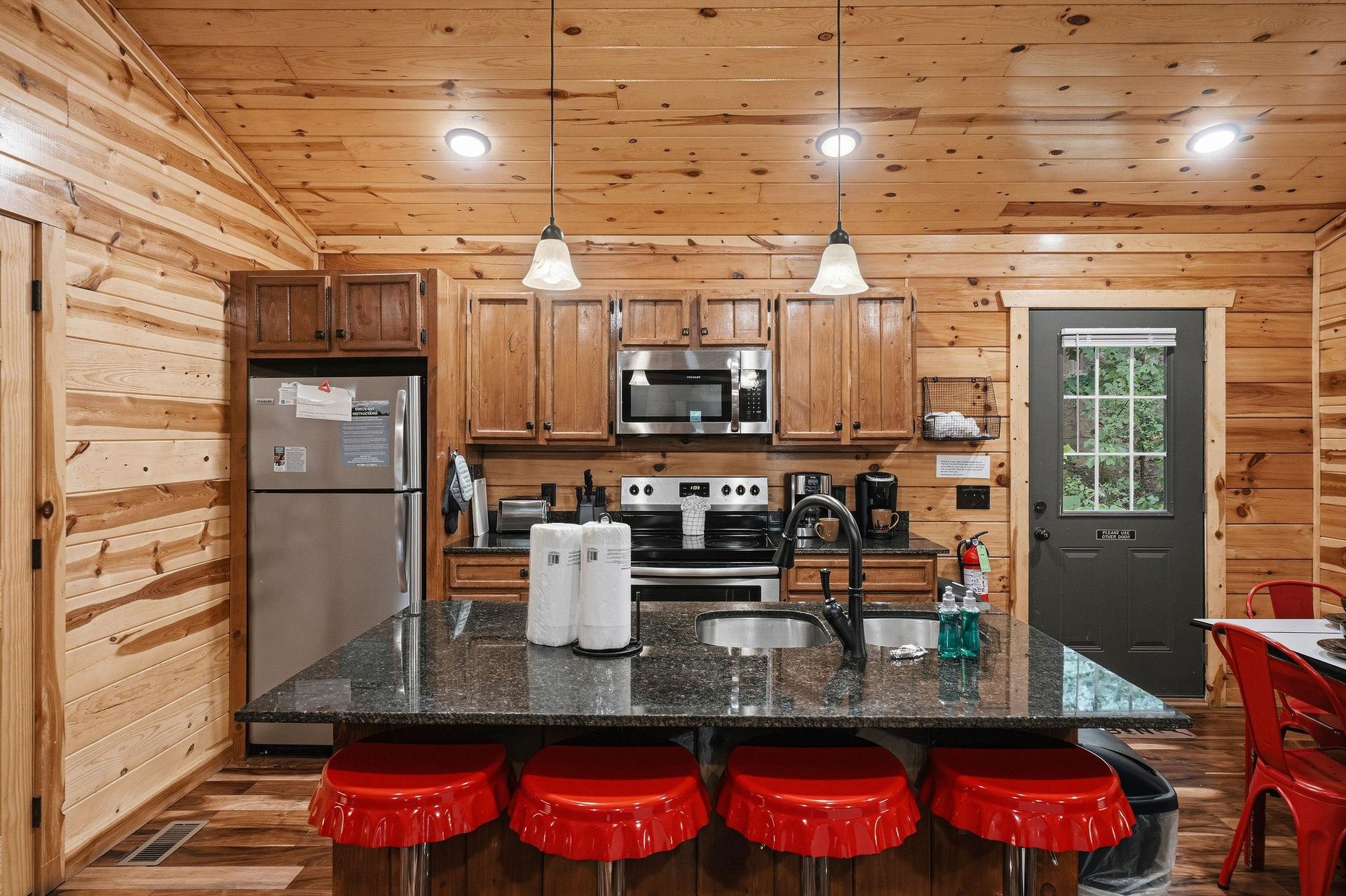 Your fully equipped kitchen is bathed in warm wood tones, ready for you to whip up your favorite meals at the sleek granite island surrounded by playful red stools.
