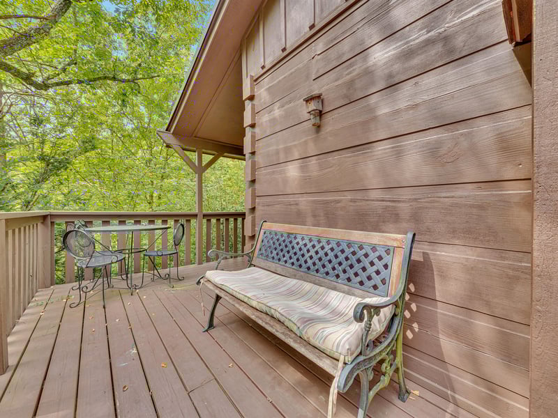 Relax on your private deck with a cushioned bench and bistro table, surrounded by lush green forest views.