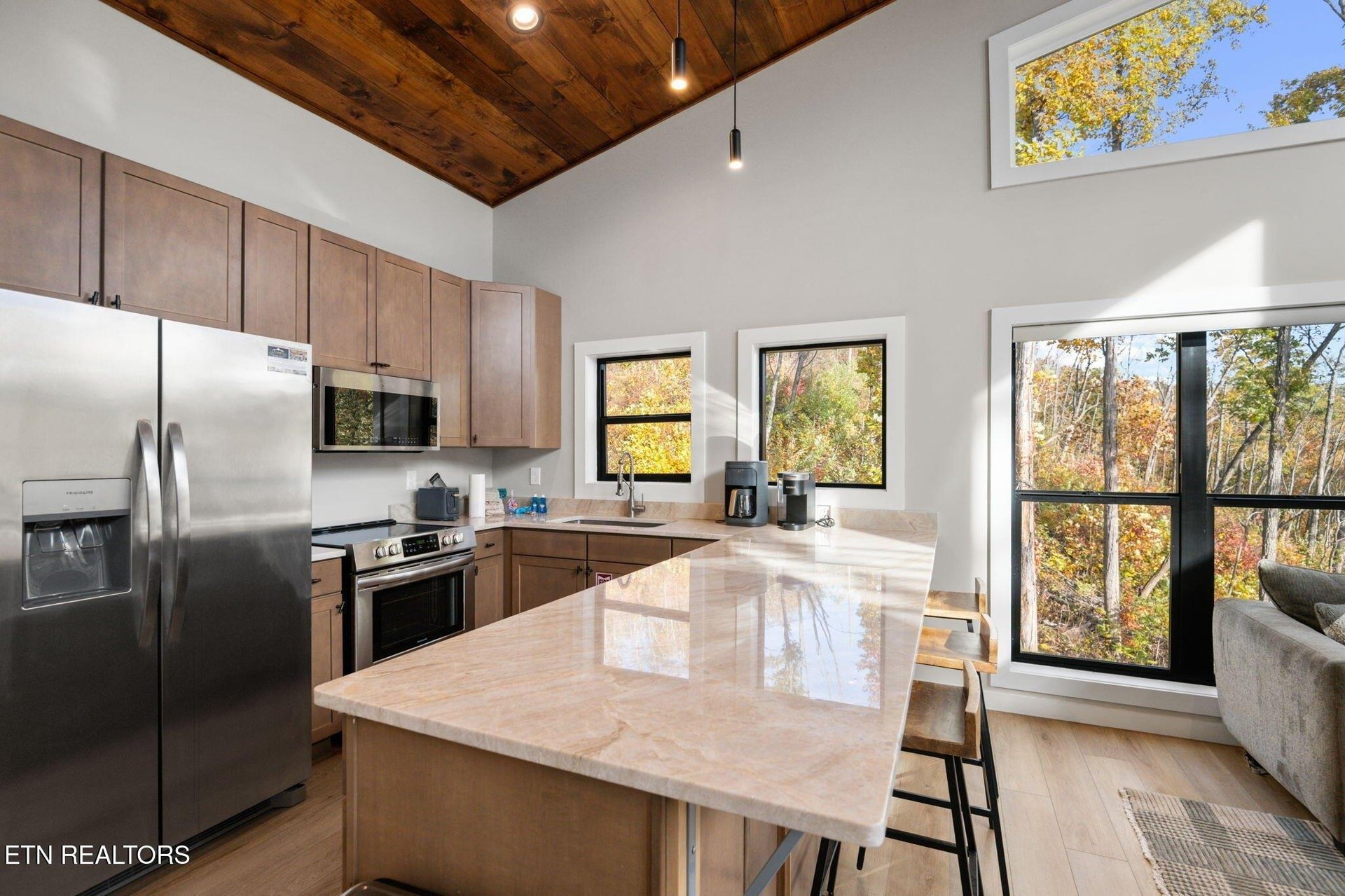 Step into your sunlit kitchen with soaring woodbeam ceilings and peaceful forest views framing every window. The bright island and modern appliances invite you to cook, gather, and soak in the natura