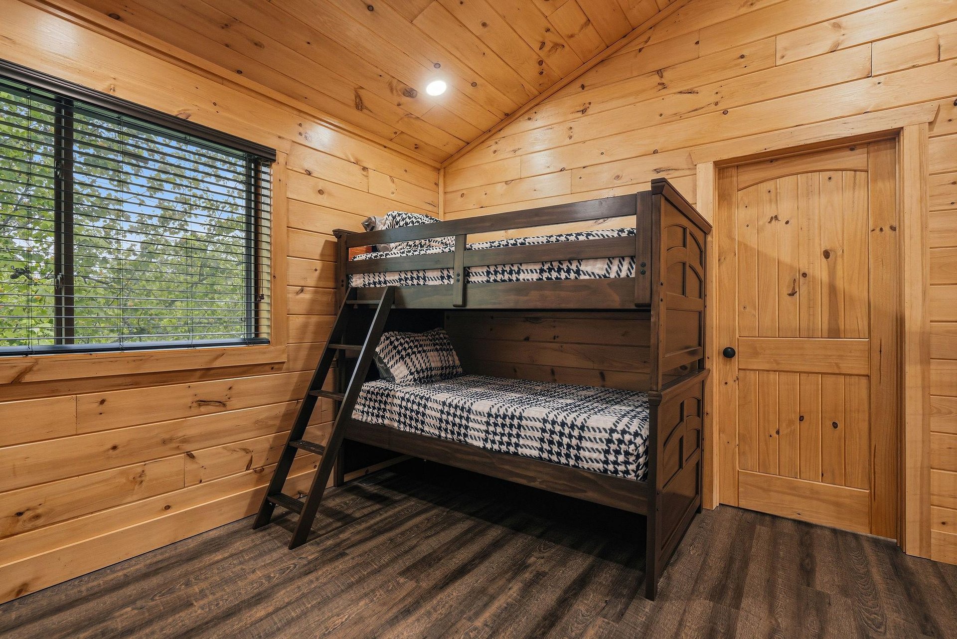 Your cozy cabin bedroom features rustic bunk beds with geometric bedding, surrounded by warm wood paneling and natural forest views.