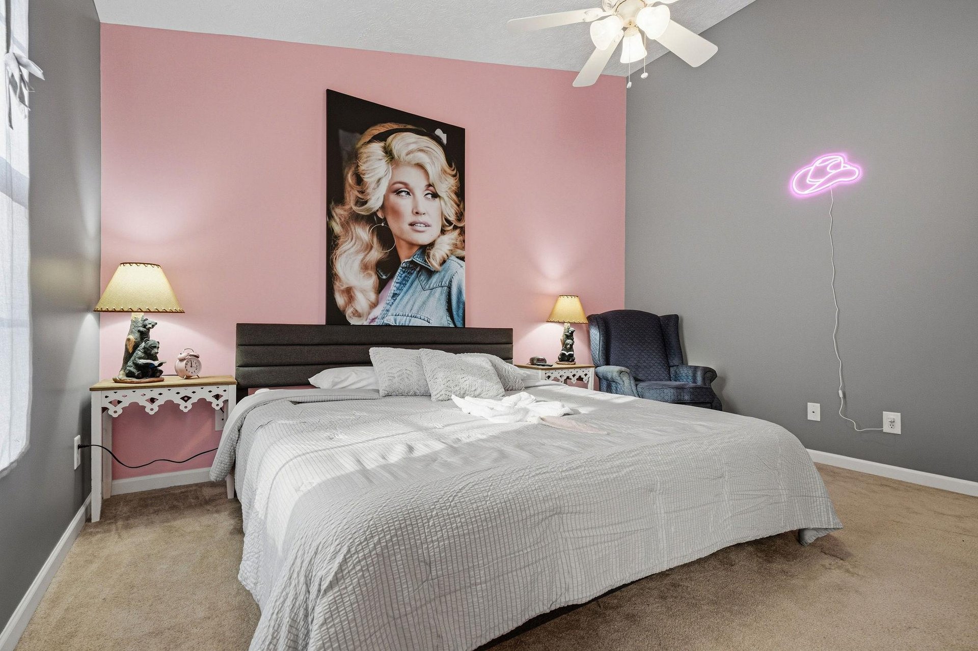 Unwind in this stylish bedroom featuring a plush queen bed, vintage nightstands, and playful neon cloud lighting that creates the perfect mood.