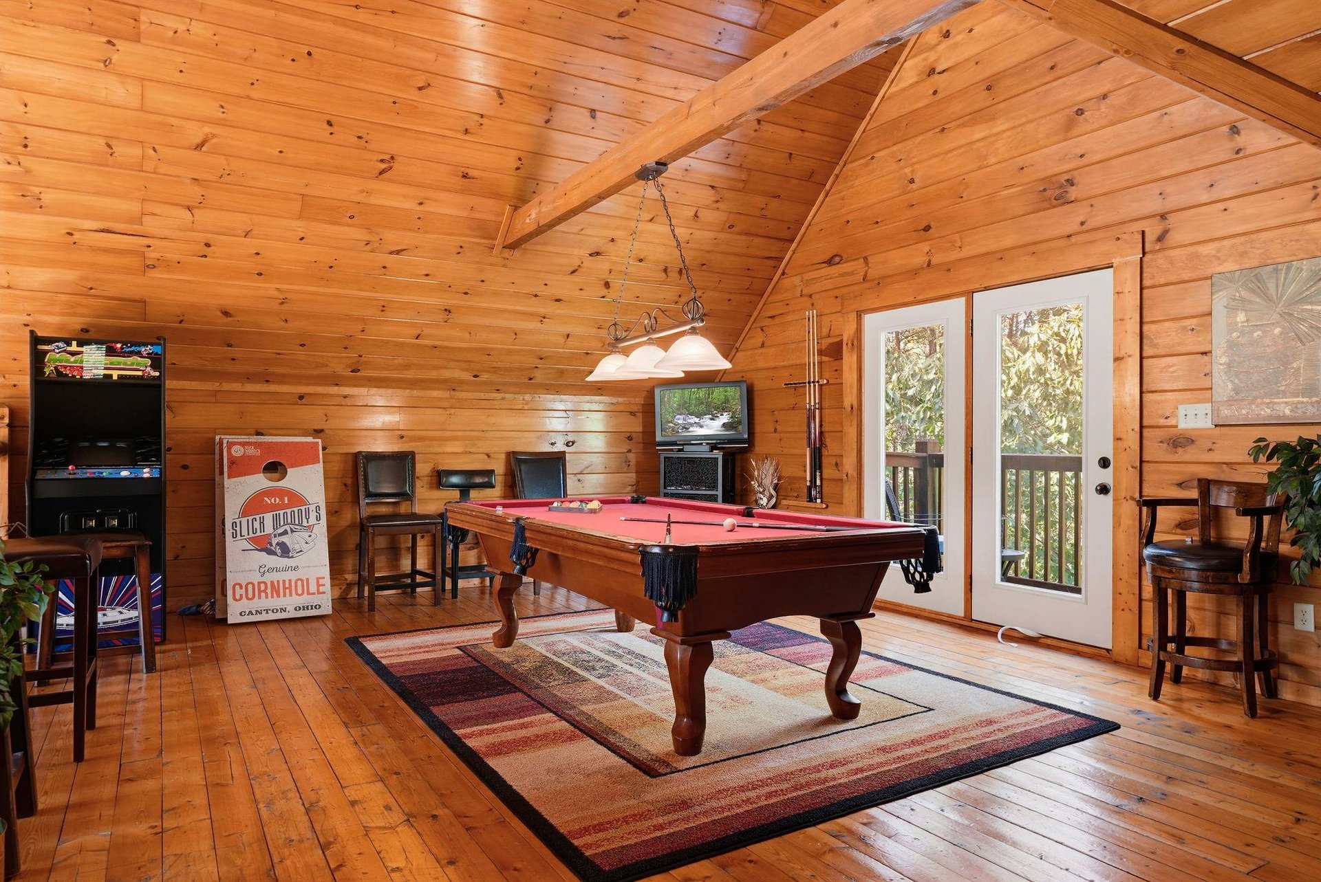 Your private game room awaits with a pool table and arcade entertainment beneath soaring timberbeam ceilings, opening onto your own balcony surrounded by trees.