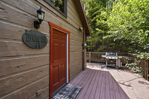Welcome to Tennessee River This inviting cabin entrance opens to a spacious deck surrounded by lush greenery, perfect for al fresco dining and grilling memorable meals.