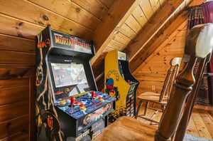 Challenge your friends to classic arcade battles in this cozy cabin loft game nook with vaulted wooden ceilings and nostalgic entertainment.