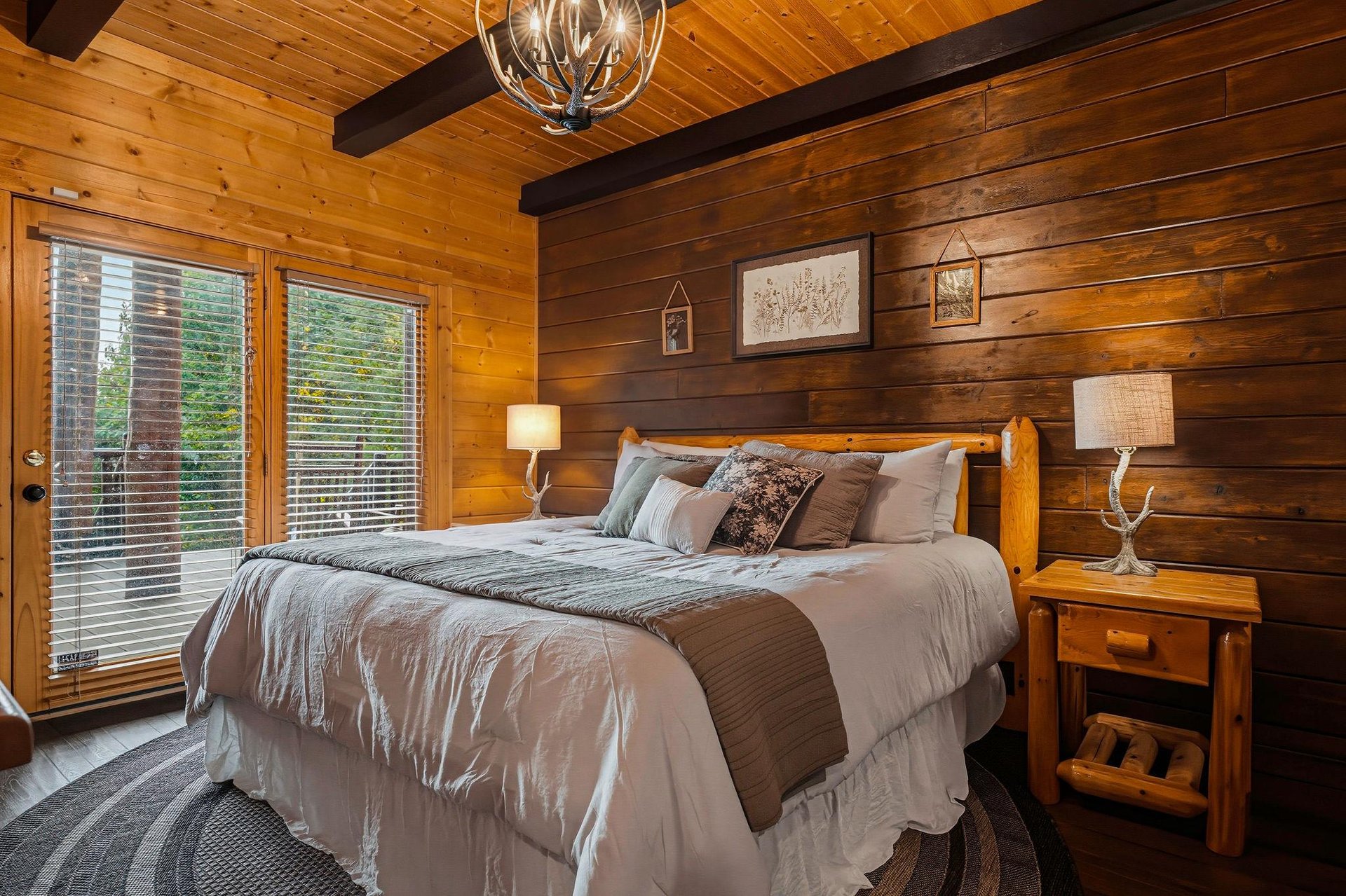 Sink into soft linens and rustic charm in this cozy bedroom, where warm wood walls and antleraccented lighting invite restful mountain evenings.