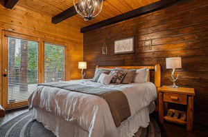 Sink into soft linens and rustic charm in this cozy bedroom, where warm wood walls and antleraccented lighting invite restful mountain evenings.