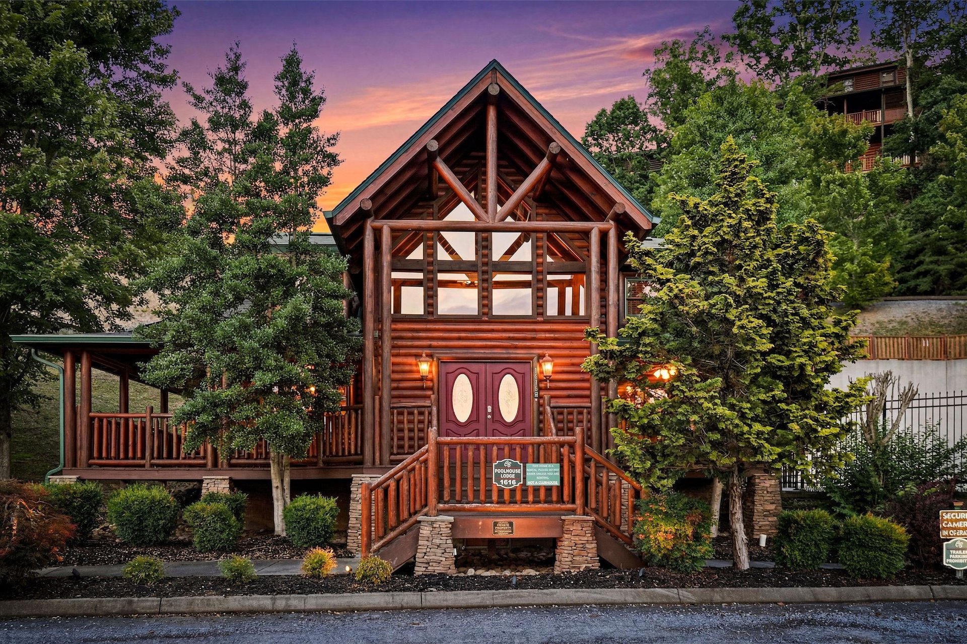 Rustic log cabin exterior features warm wood tones and charming architecture, nestled among evergreens beneath a stunning sunset sky in a peaceful mountain neighborhood.