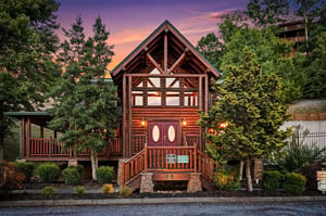 Rustic log cabin exterior features warm wood tones and charming architecture, nestled among evergreens beneath a stunning sunset sky in a peaceful mountain neighborhood.