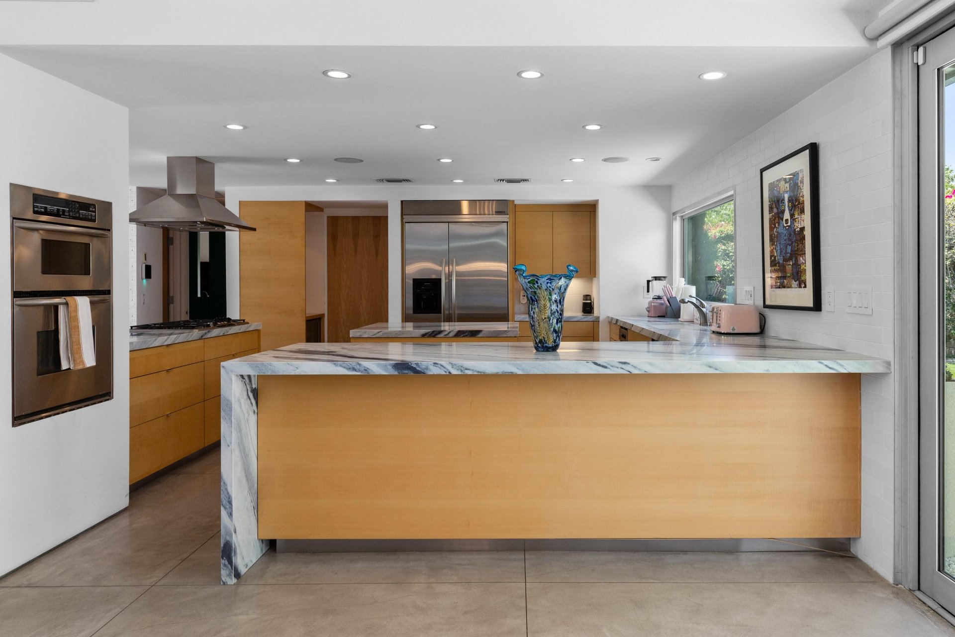 Modern chefs kitchen with a waterfall marble counter, kitchen island, stainlesssteel appliances, wine fridge, wet bar, and kitchen essentials.