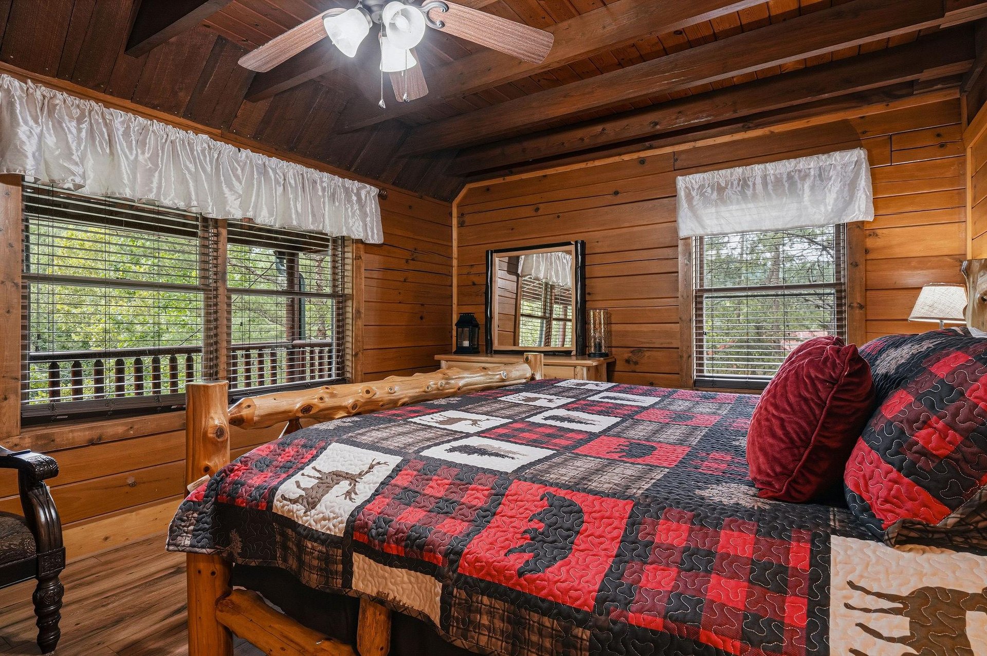 Drift off in this cozy bedroom with rustic log furniture, warm woodpaneled walls, and windows framing leafy views. Your comfortable retreat awaits.