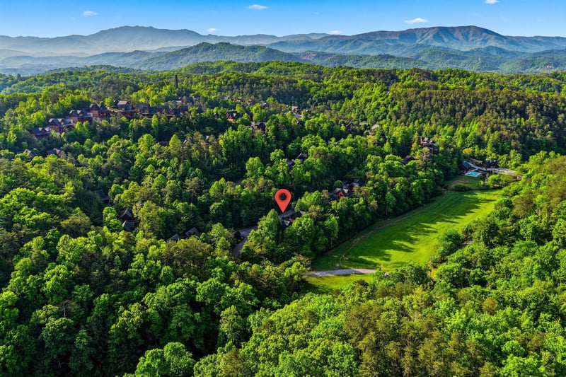 Aerial view showcases the propertys location within a lush mountain landscape, nestled among rolling hills and verdant forests.