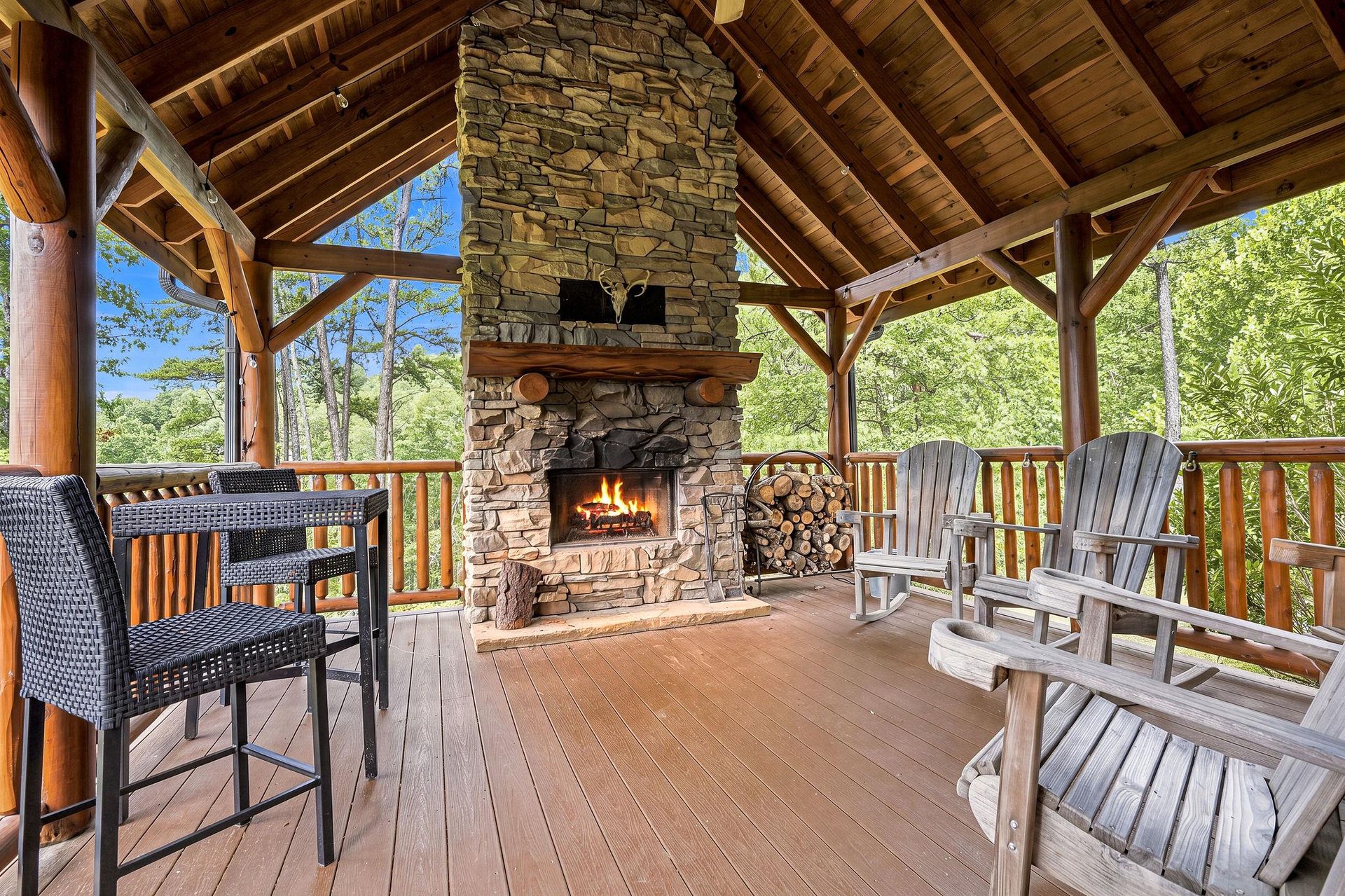 Gather around your own stone fireplace on this covered deck, with Adirondack chairs and forested views all around—perfect for cozy mountain evenings.