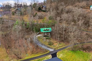 Charming cabin with distinctive green roof nestled among rolling hills and winding country roads in a peaceful wooded neighborhood.
