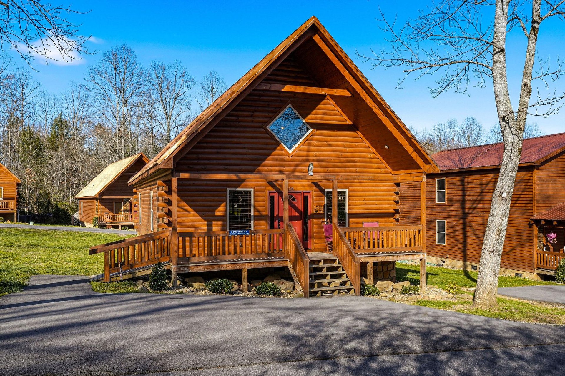A charming log cabin featuring rustic wood construction with a distinctive diamond window accent and welcoming front deck.