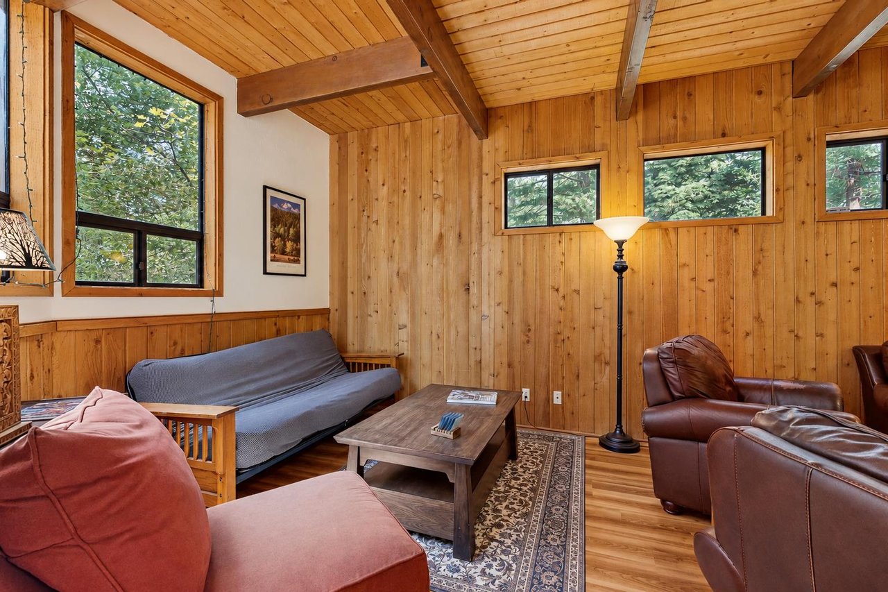 A relaxed second seating nook off the main living area, with knotty pine walls and forest views. The futon doubles as an extra sleeping spot for the group — just ask and well have sheets ready for it.