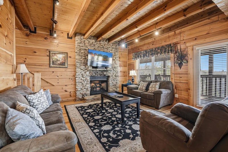 Sink into plush seating by the crackling stone fireplace, where rustic wood beams frame your mountain retreat moments perfectly.