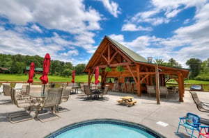 This inviting timber pavilion frames your outdoor space, with multiple lounging spots, picnic tables, and red umbrellas—all set against lush lawns and open skies perfect for a relaxing afternoon.
