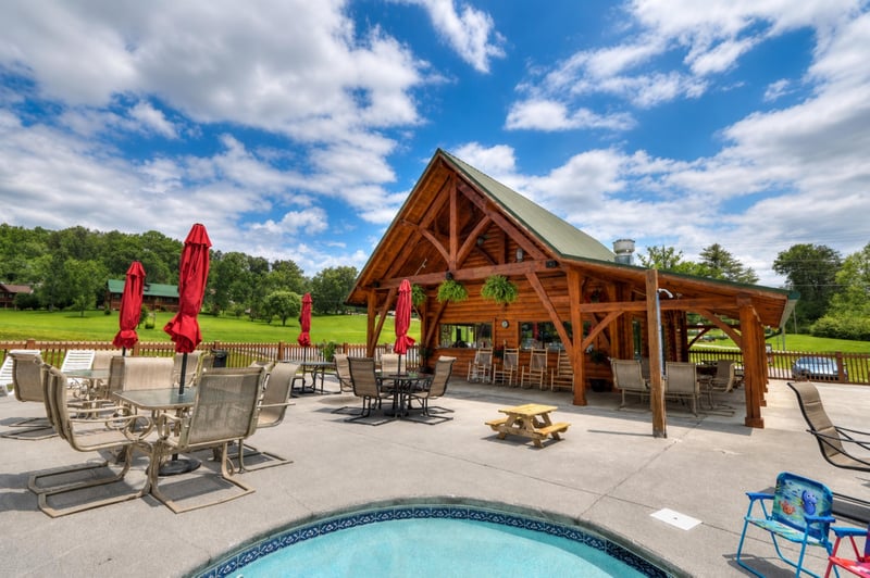 This inviting timber pavilion frames your outdoor space, with multiple lounging spots, picnic tables, and red umbrellas—all set against lush lawns and open skies perfect for a relaxing afternoon.