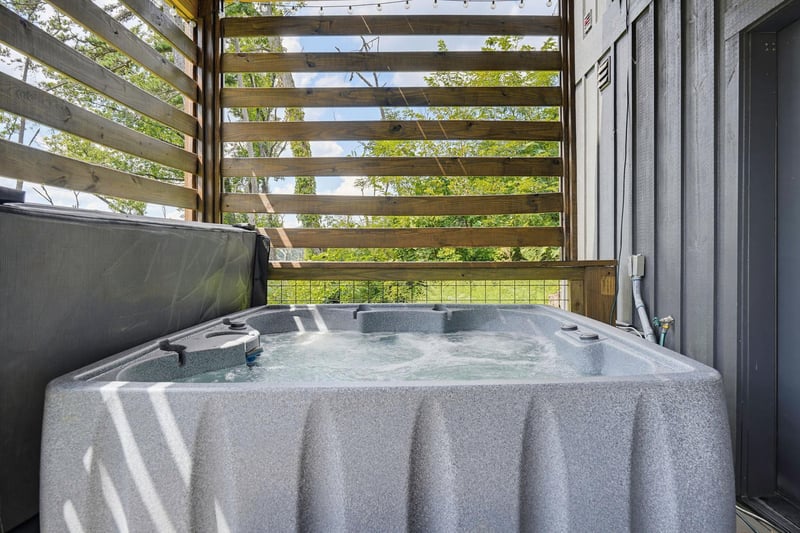 Soak away your cares in your own private hot tub, nestled on a charming wooden terrace surrounded by lush greenery and dappled sunlight.
