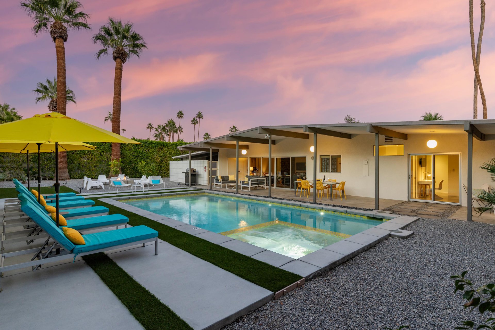 Modern desert oasis with sparkling pool surrounded by towering palms, captured at twilight with stunning pinkpurple sky overhead.