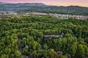 Stunning aerial view of the property nestled among lush forests with mountain backdrop and city views at sunset.