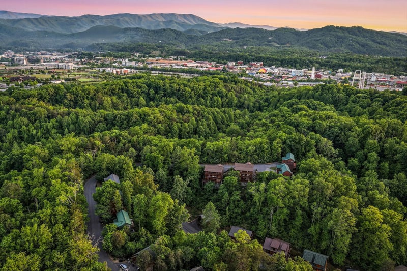 Stunning aerial view of the property nestled among lush forests with mountain backdrop and city views at sunset.