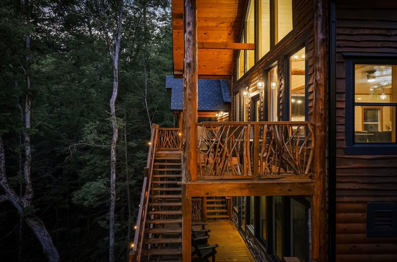 Rustic wood cabin exterior with handcrafted twig railings and warmlit interiors illuminates the serene forest setting at twilight.