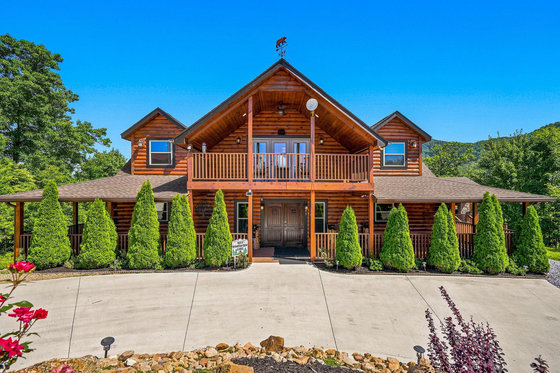 Stunning log cabin exterior showcasing classic craftsmanship, nestled among lush greenery with a spacious driveway and manicured landscaping—a welcoming retreat in a peaceful natural setting.