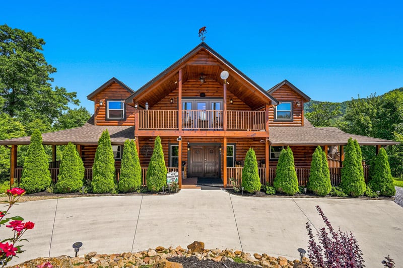 Stunning log cabin exterior showcasing classic craftsmanship, nestled among lush greenery with a spacious driveway and manicured landscaping—a welcoming retreat in a peaceful natural setting.