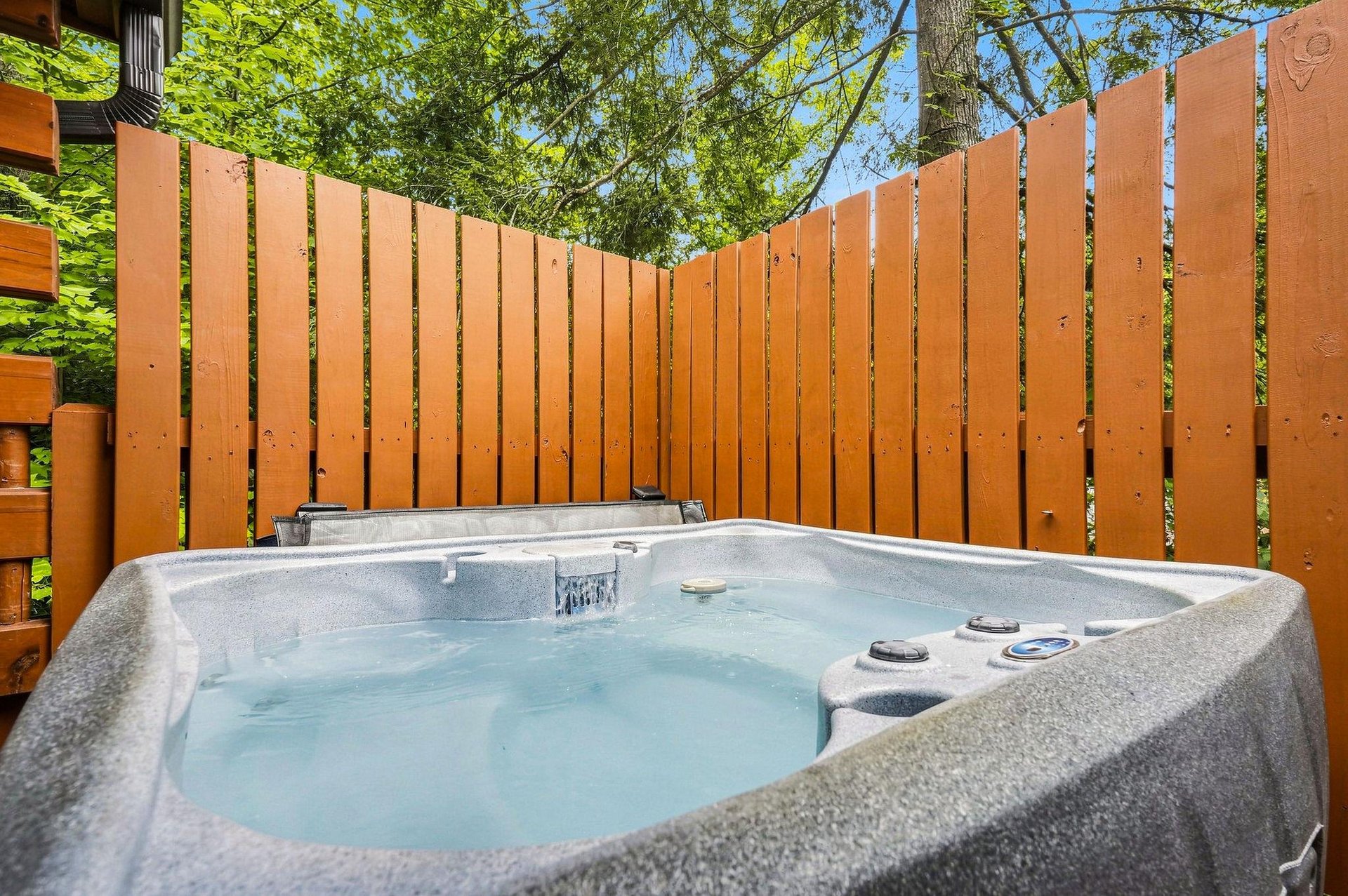 Slip into your own private hot tub, tucked away behind tall wooden fencing. Surrounded by lush greenery and a canopy of trees, its your quiet escape for soaking under open sky.