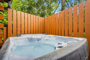 Slip into your own private hot tub, tucked away behind tall wooden fencing. Surrounded by lush greenery and a canopy of trees, its your quiet escape for soaking under open sky.