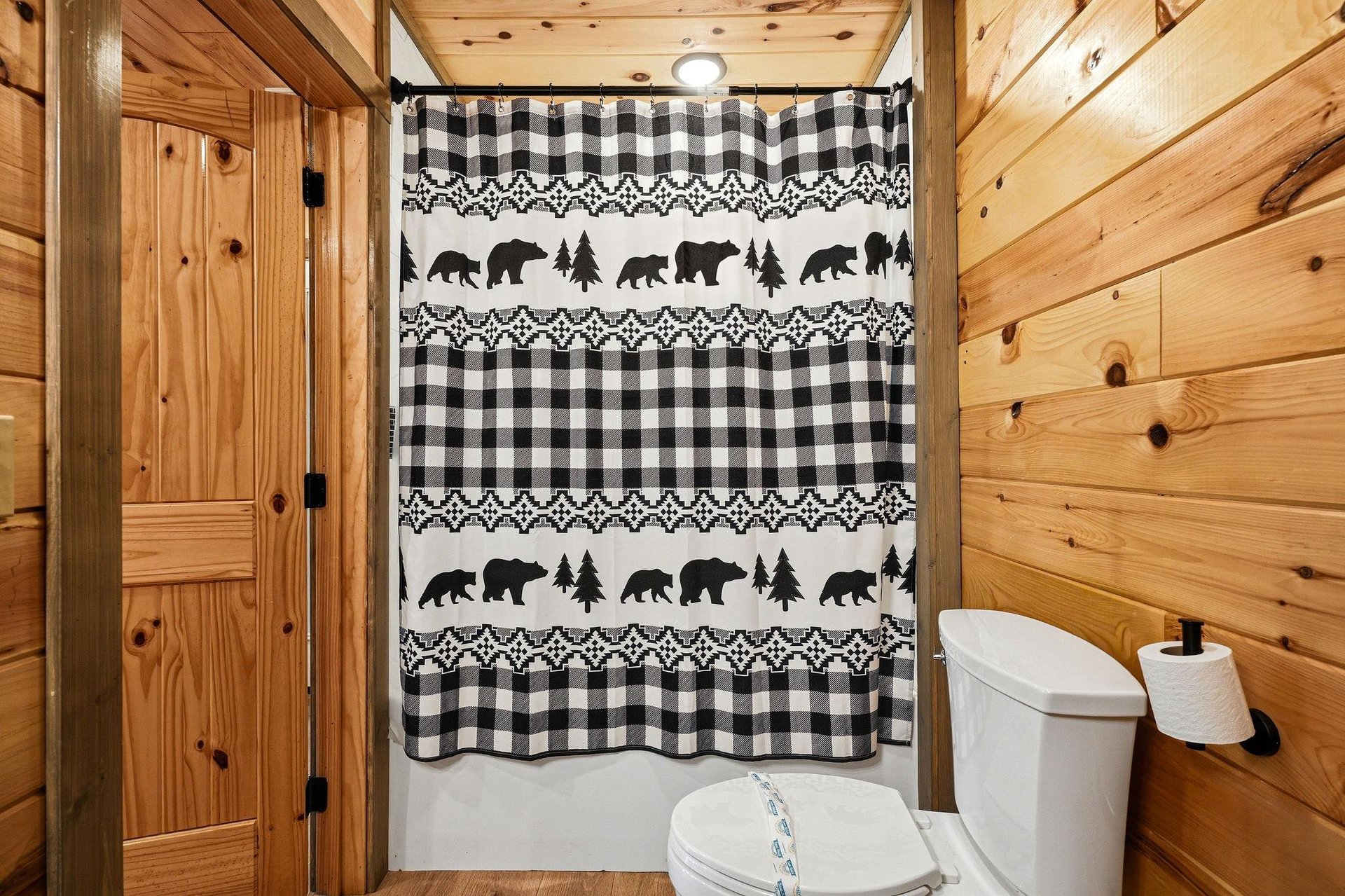Your rustic bathroom features warm wood paneling and charming bearthemed shower curtain for an authentic cabin experience.