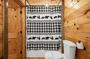 Your rustic bathroom features warm wood paneling and charming bearthemed shower curtain for an authentic cabin experience.